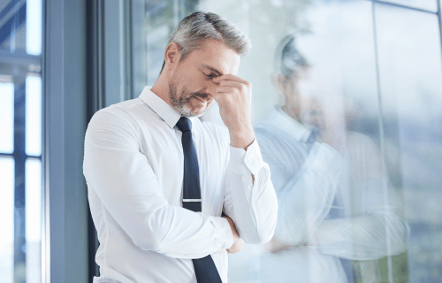 A stressed man in formal attire standing close to a meeting room window