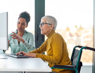 An older woman employee in a wheelchair discussing work with a coworker.