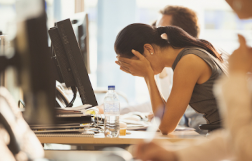 Stressed employee at work desk with hands covering her face.