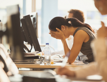 Stressed employee at work desk with hands covering her face.