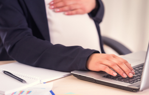 A pregnant employee working on a laptop