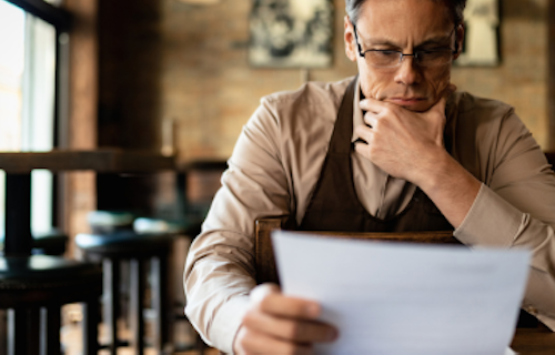 A small business owner sitting in his cafe and reading about the new changes under Bill 30