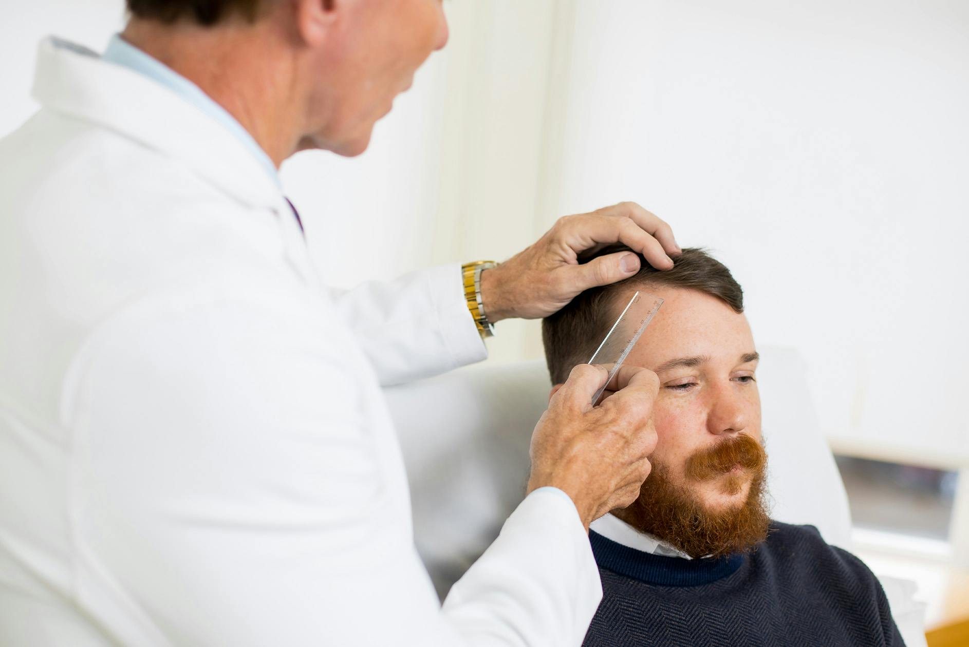 doctor examining male patient's hairline