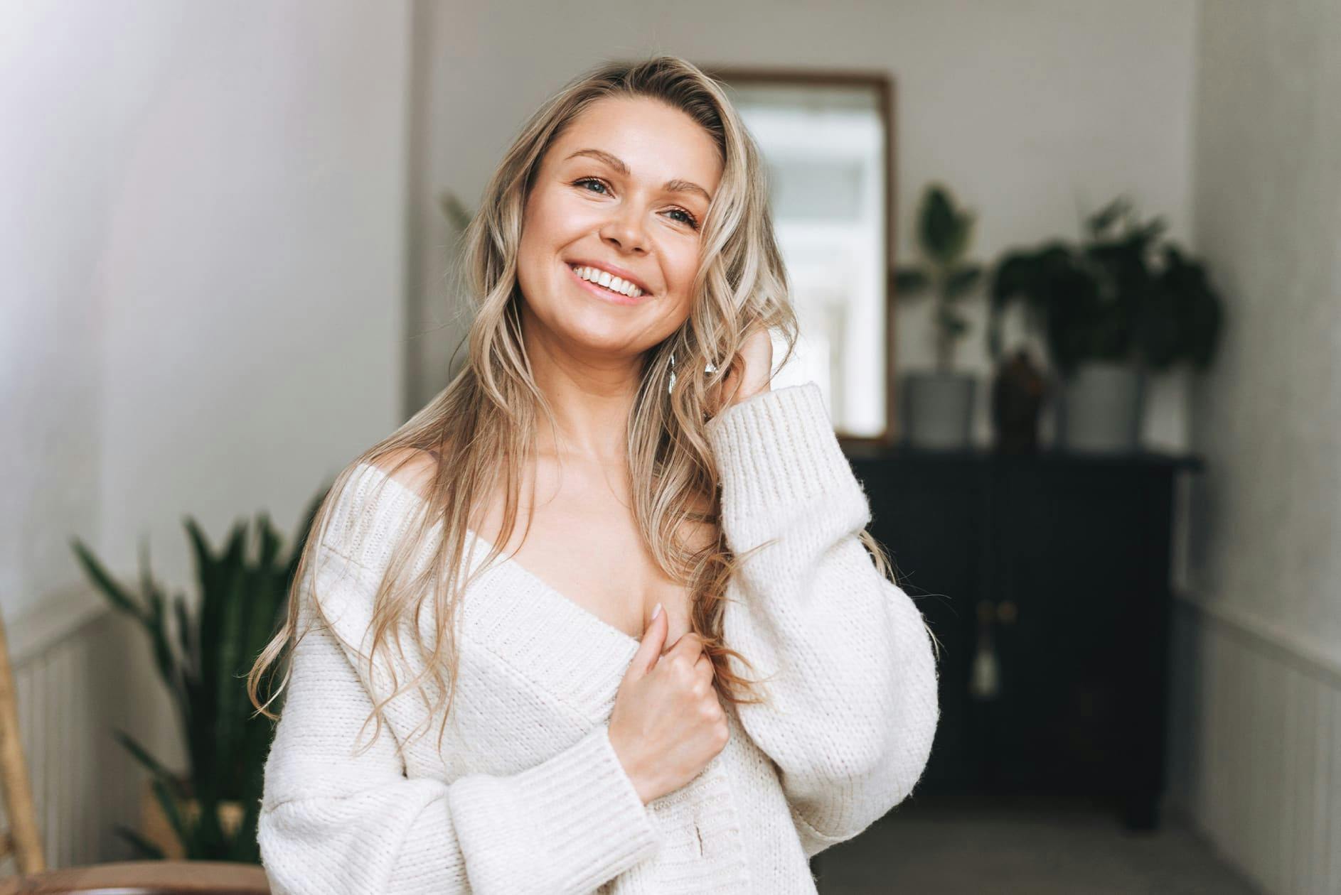 woman in white sweater while touching her hair and smiling