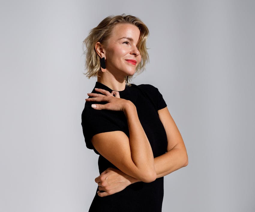 woman with short blonde hair and her hand on her own shoulder