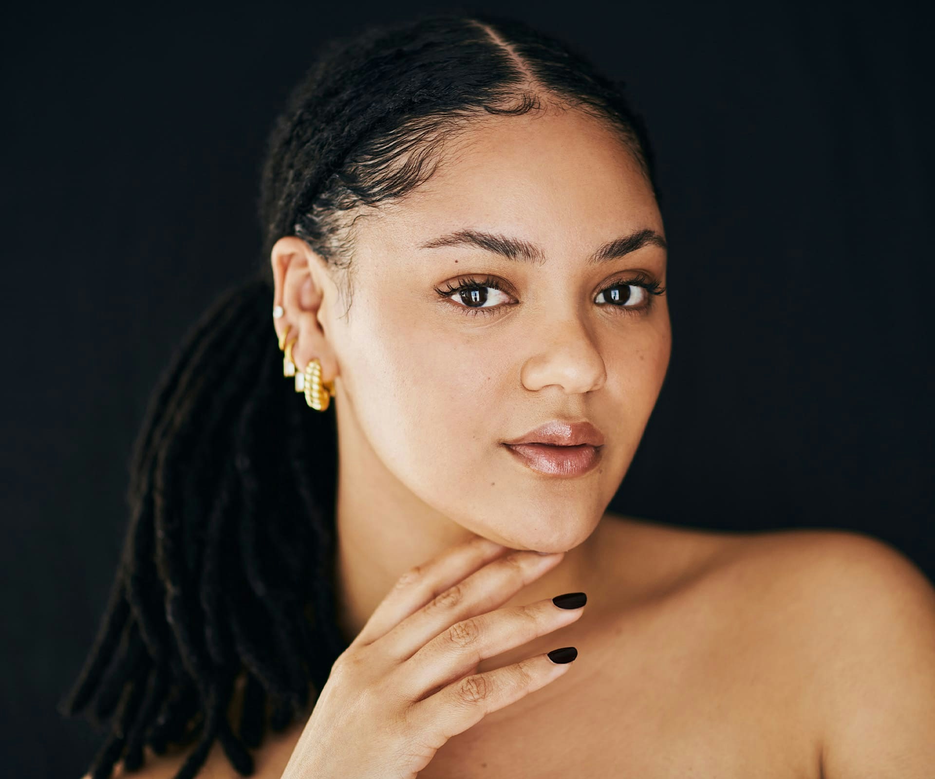 womans with dreads in a ponytail and her hand under her chin