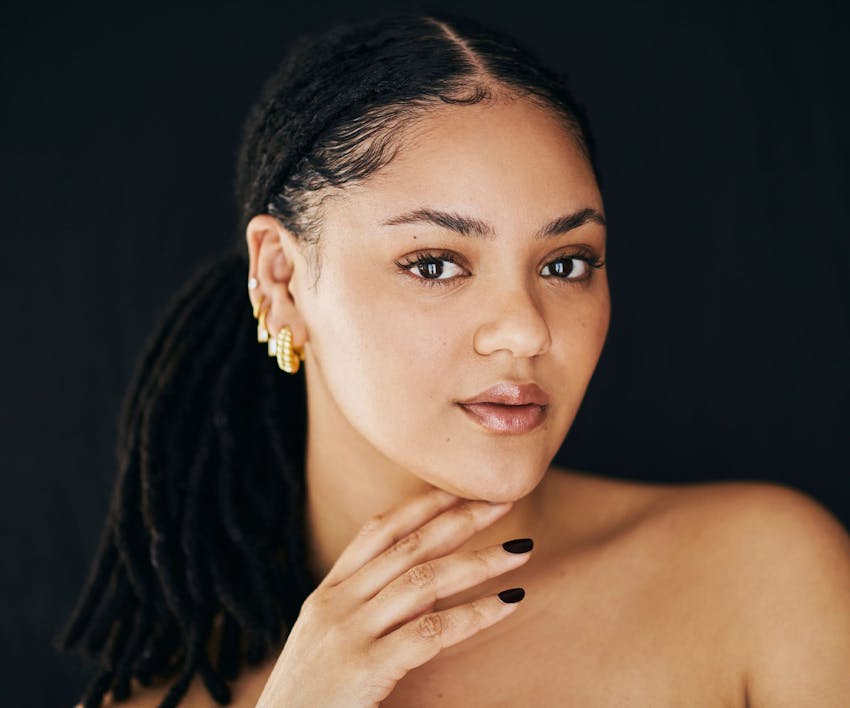 womans with dreads in a ponytail and her hand under her chin