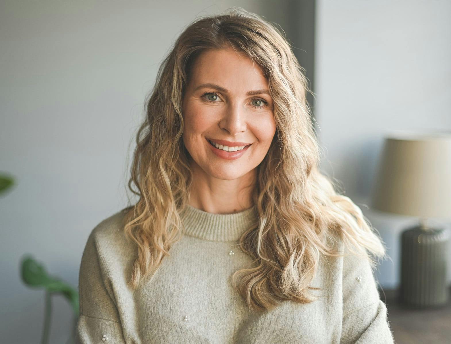 woman with blonde wavy hair smiling forward in beige sweater
