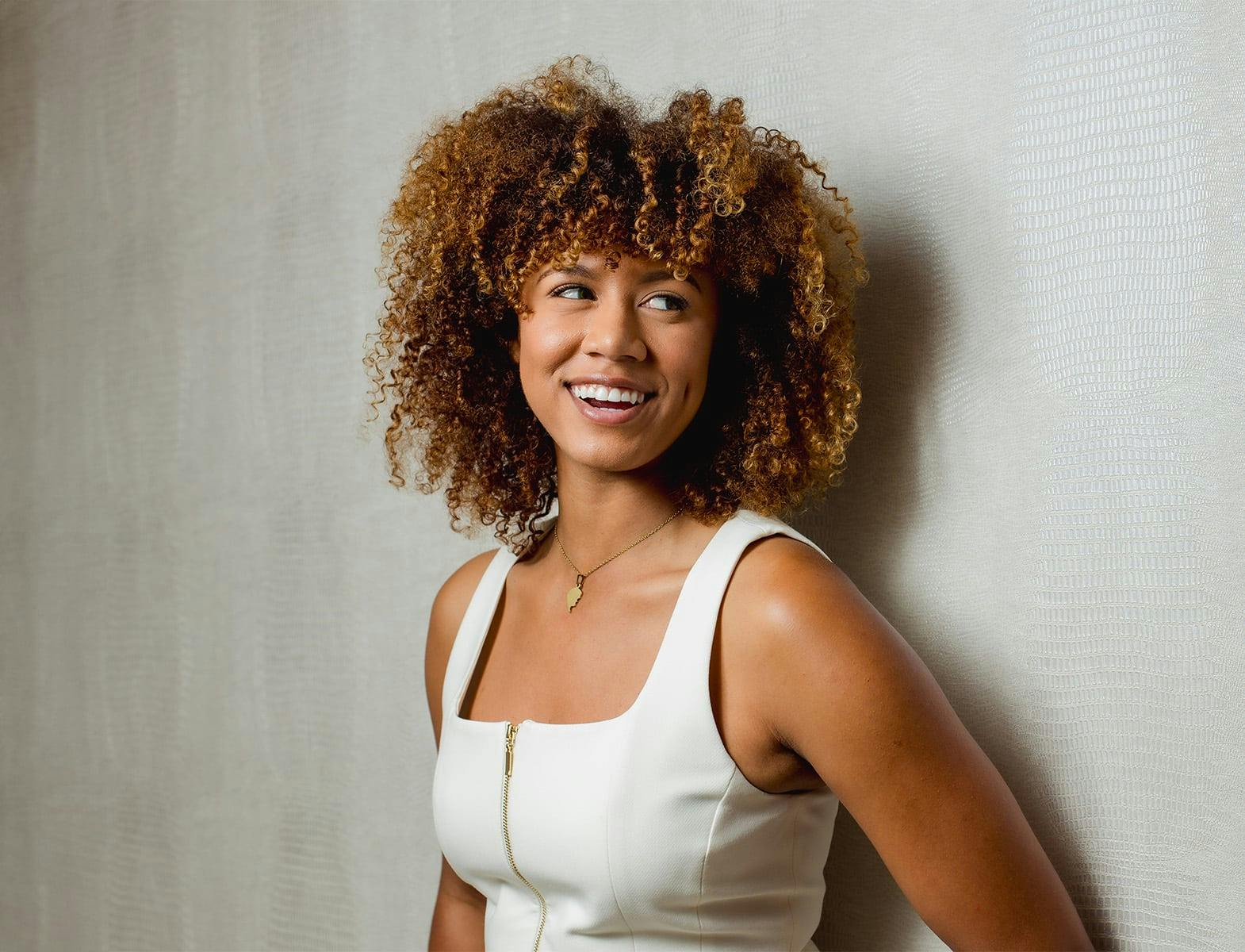woman with afro smiling and leaning against wall