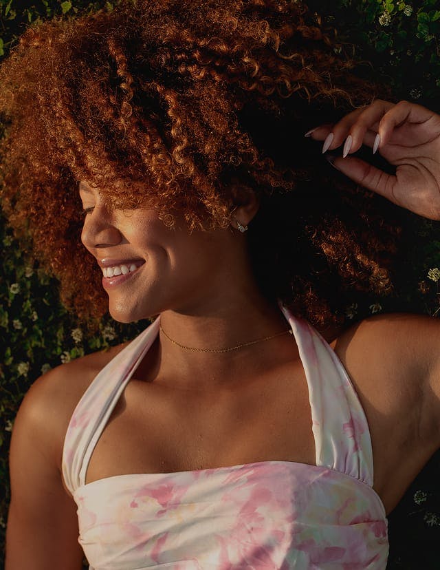Woman with curly hair smiling and touching her head