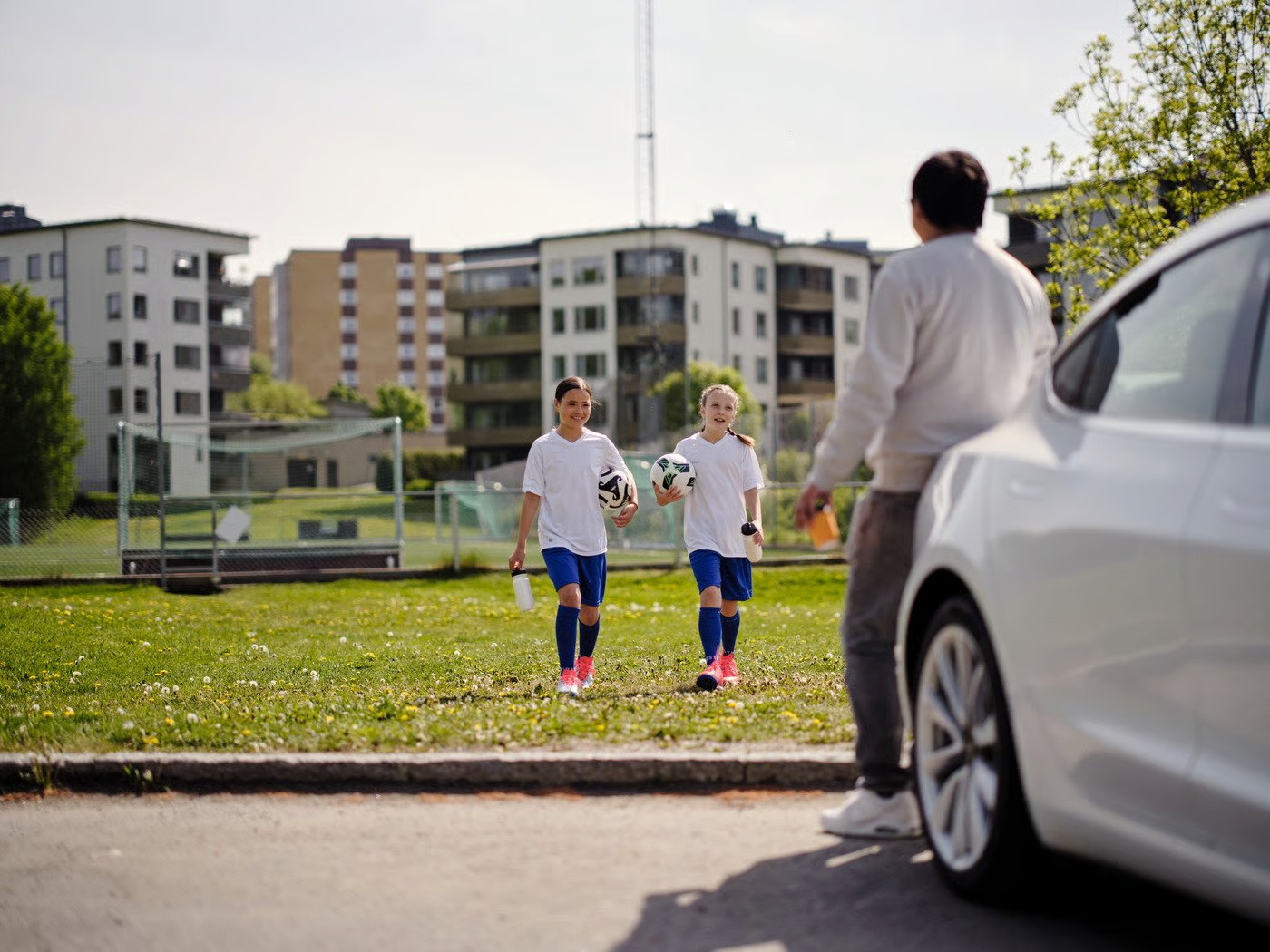 Två fotbollstjejer går med fotboll mot väntande förälder