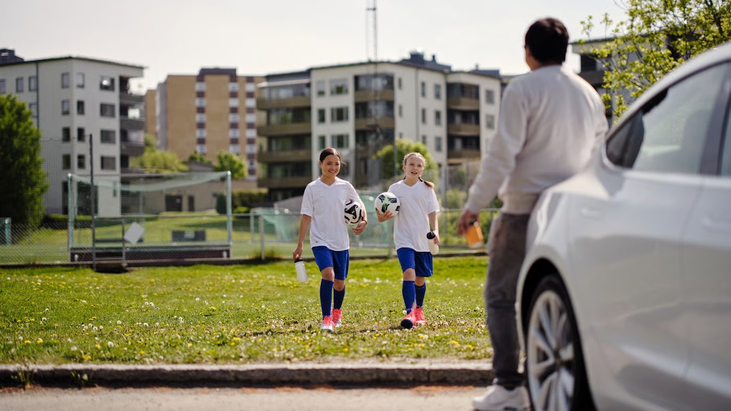 Två fotbollstjejer går med fotboll mot väntande förälder