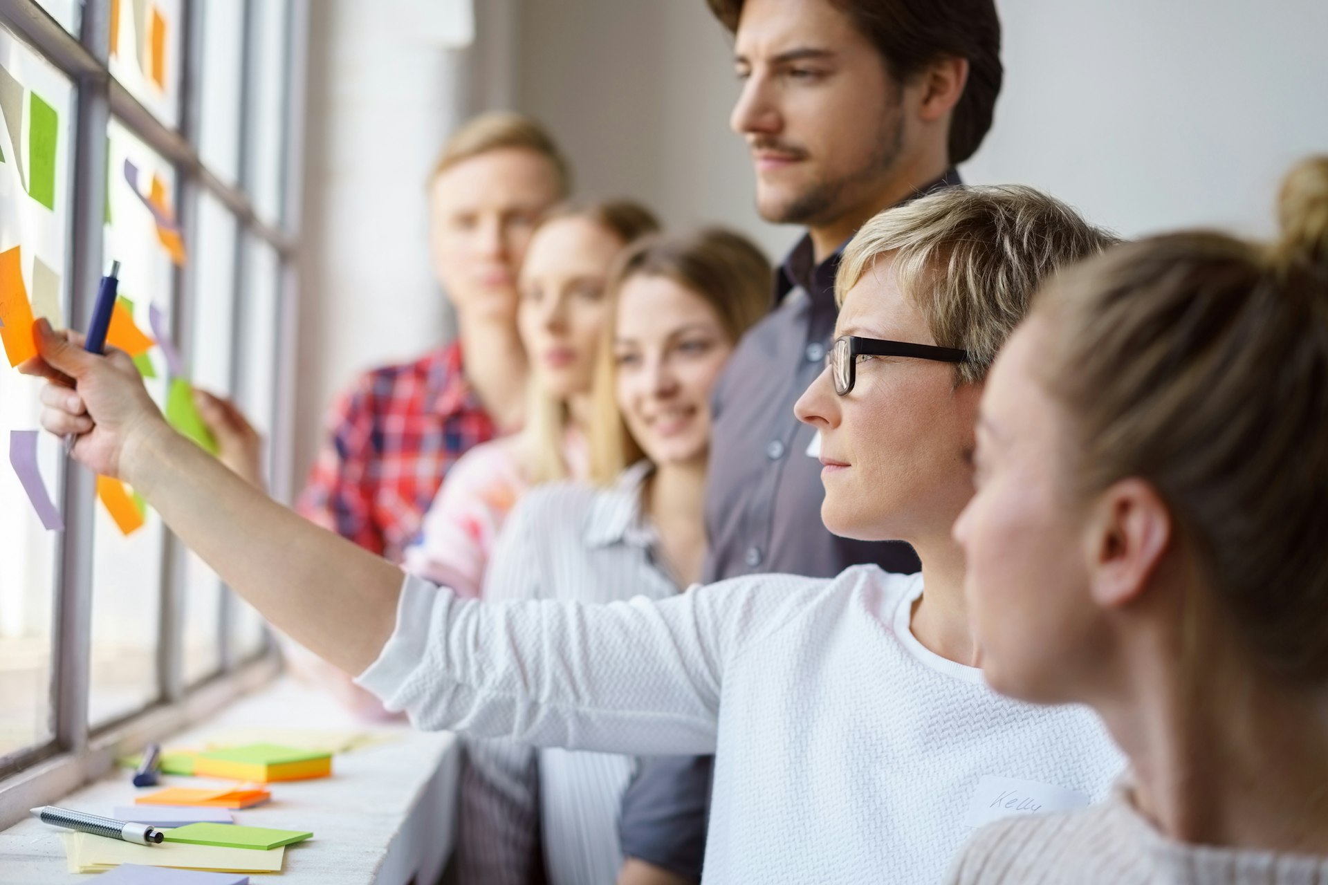 Eine Frau klebt ein Post-it an eine Wand und eine Gruppe von Menschen schauen zu.