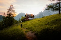 A person hikes towards a house in the mountains.