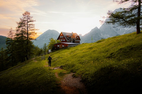 A person hikes towards a house in the mountains.