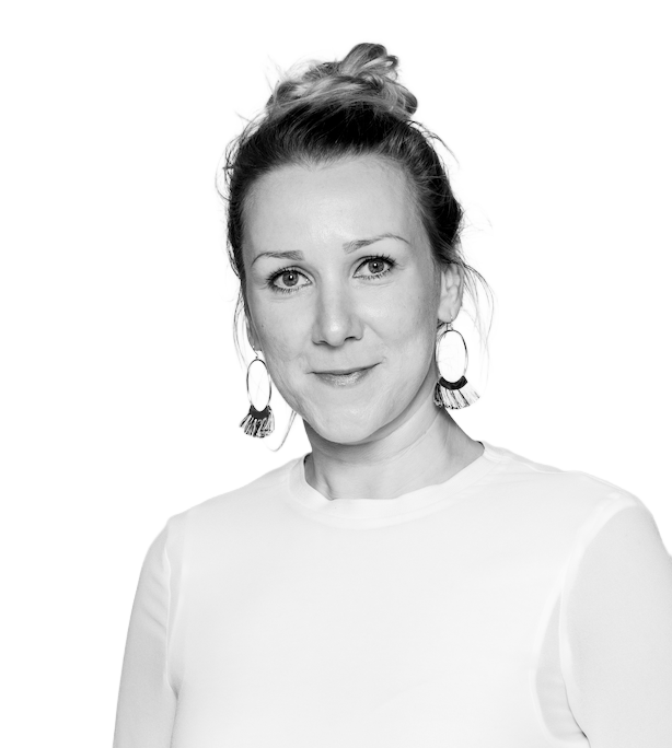 Black and white portrait of a woman with light hair in a bun, wearing large earrings and a plain long-sleeve top, looking at the camera with a neutral expression.