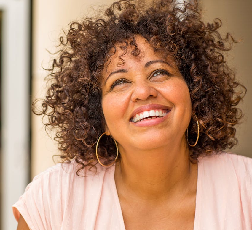 woman with curly hair in pink blouse, looking upward