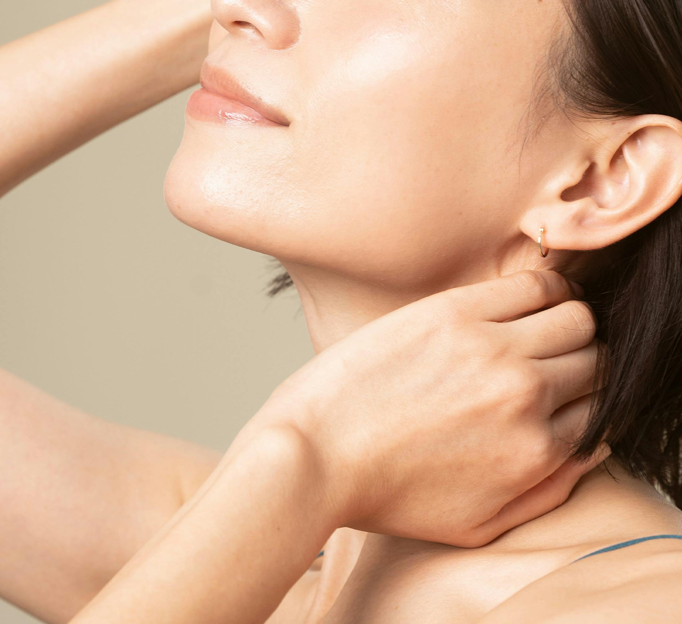 Close up of woman's neck and chin with her hands brushing back her hair