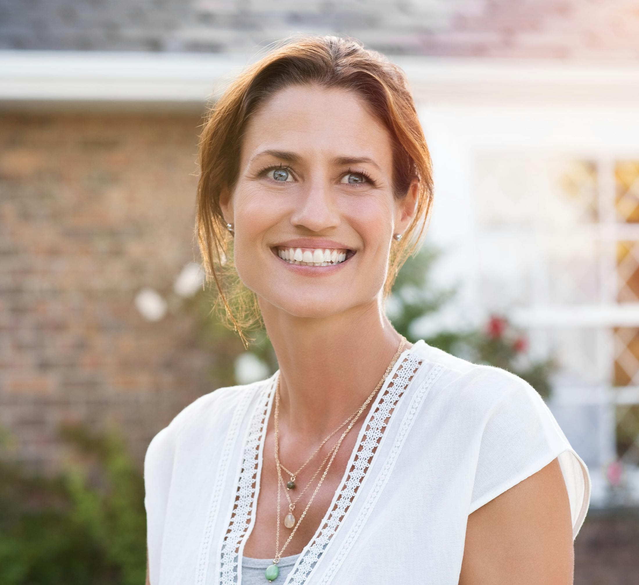 woman with hair back smiling in white top outside