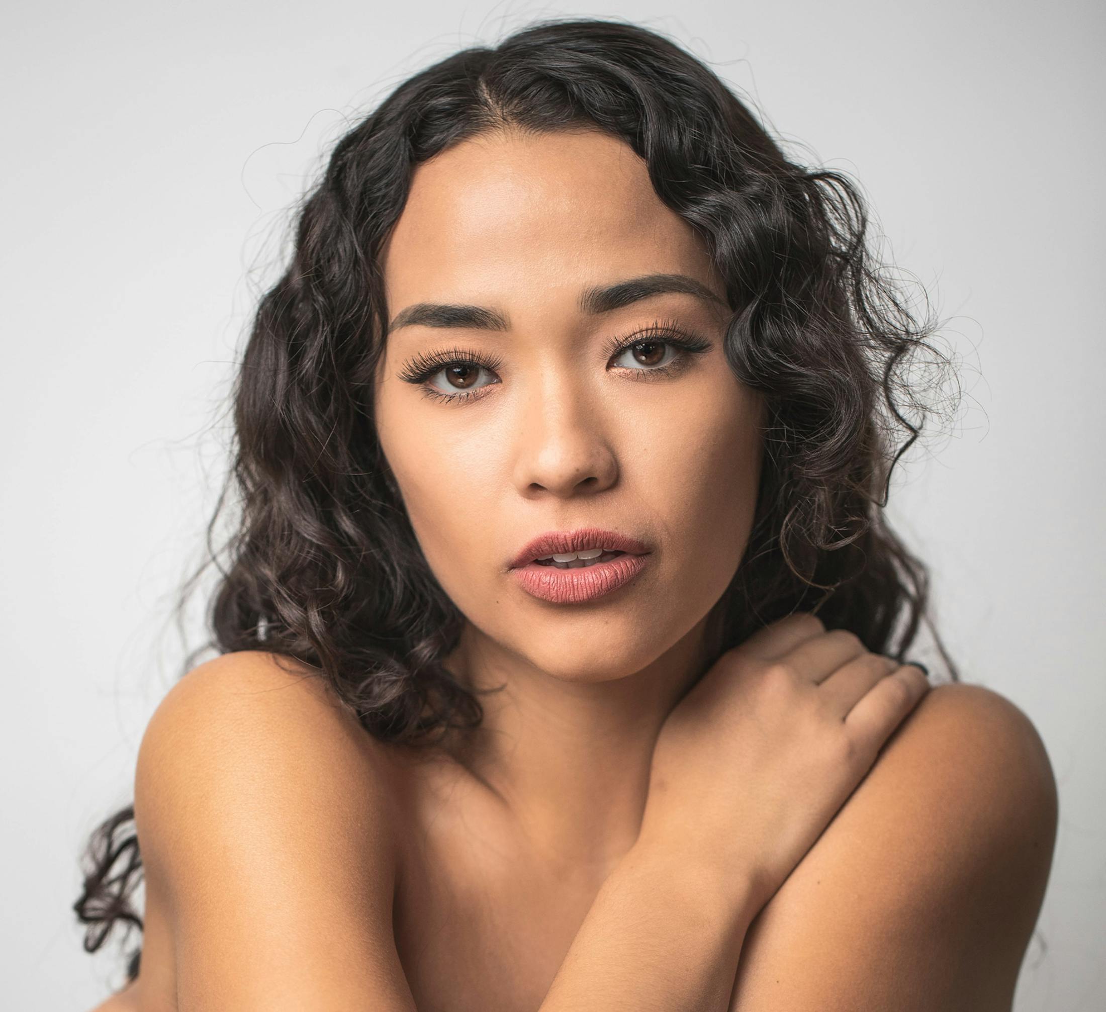 woman with curly hair looking forward, wrapping her arms around herself
