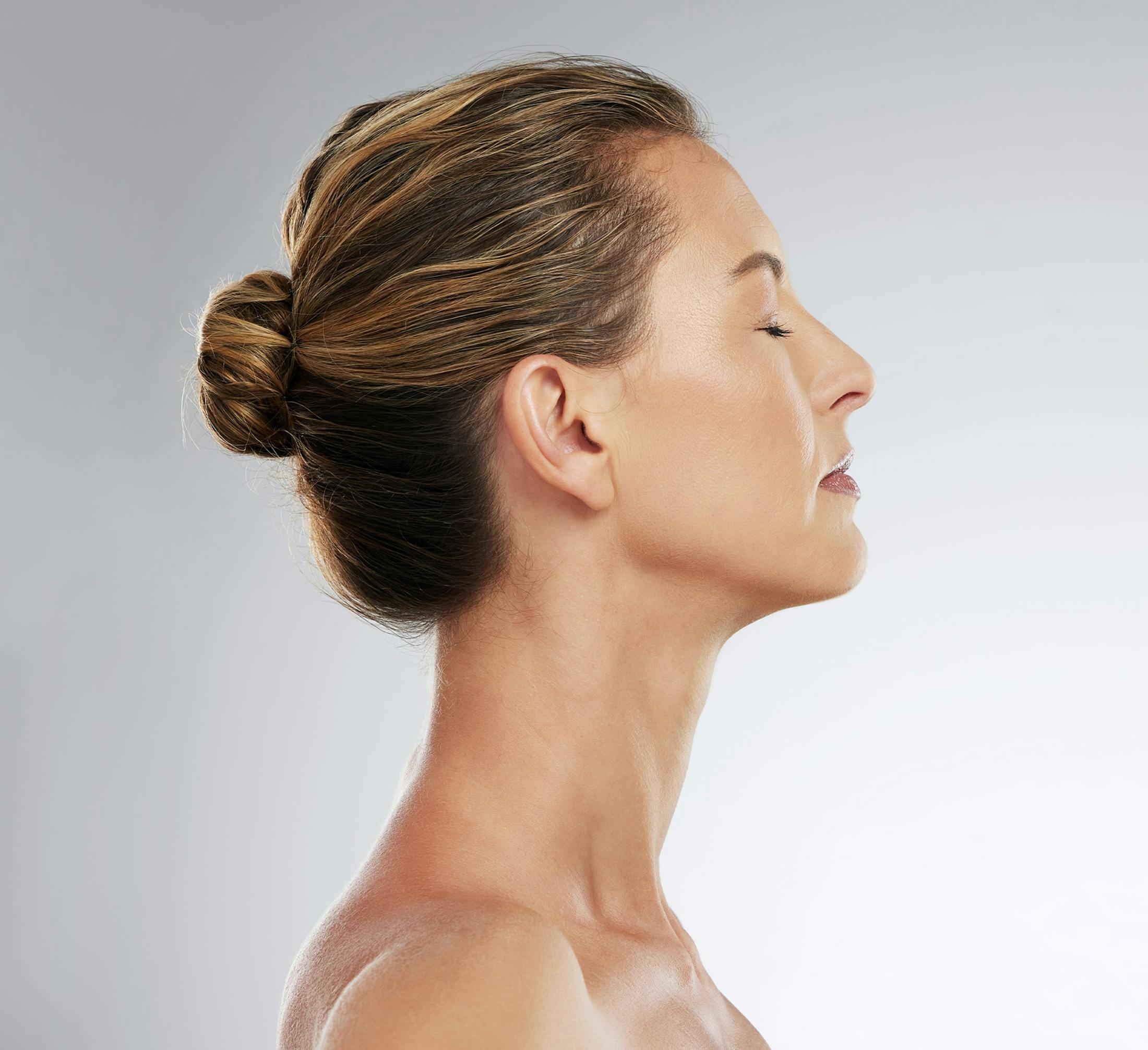 side profile of woman with hair in a bun, closed eyes, and head tilted up,