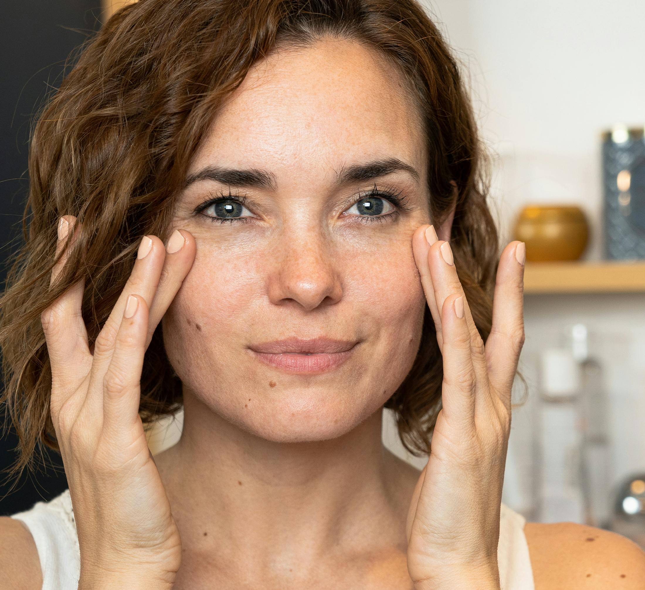 woman with short curly hair placing both hands on her cheekbones