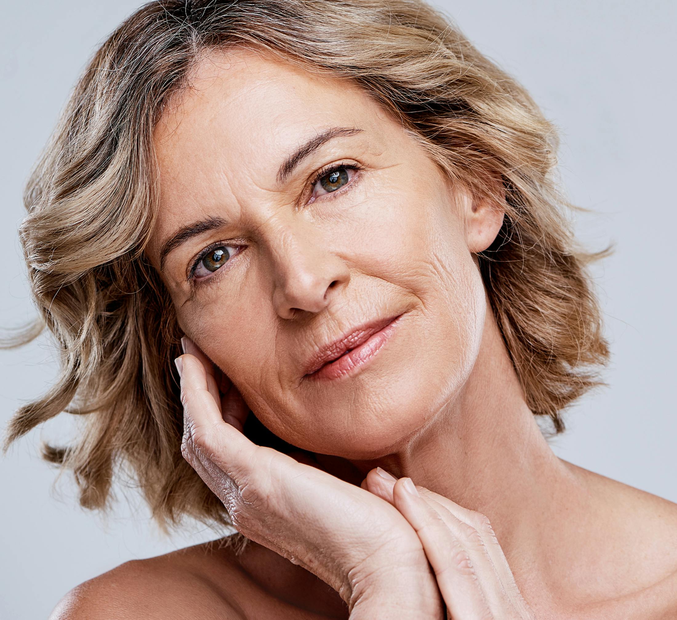 woman with short curled bob touching her cheekbone