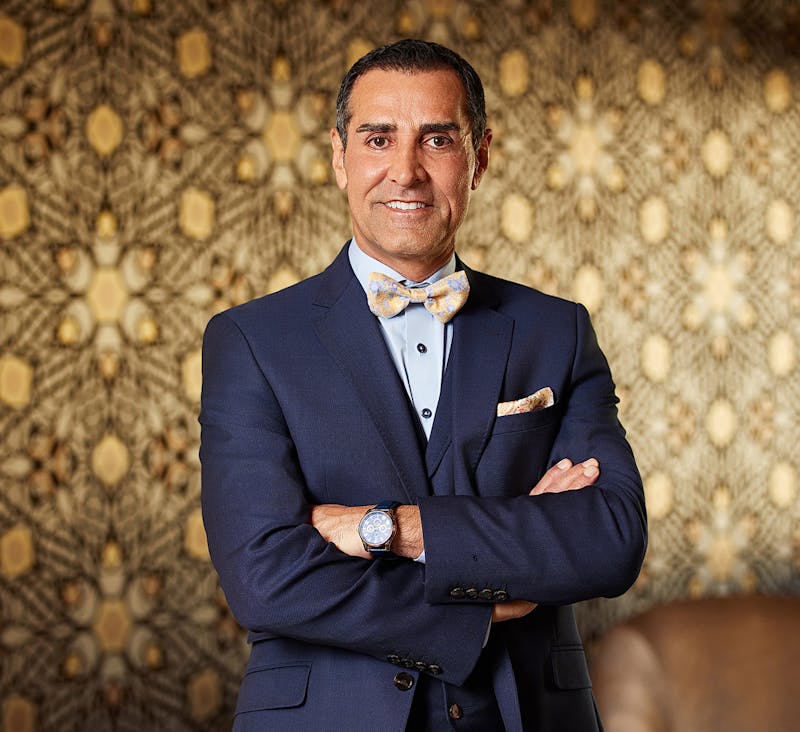 Dr. Kevin Sadati in front of a patterned wall with his arms crossed in a navy suit