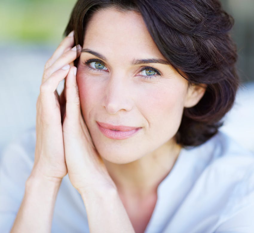 woman with short brown hair with her hands next to her face