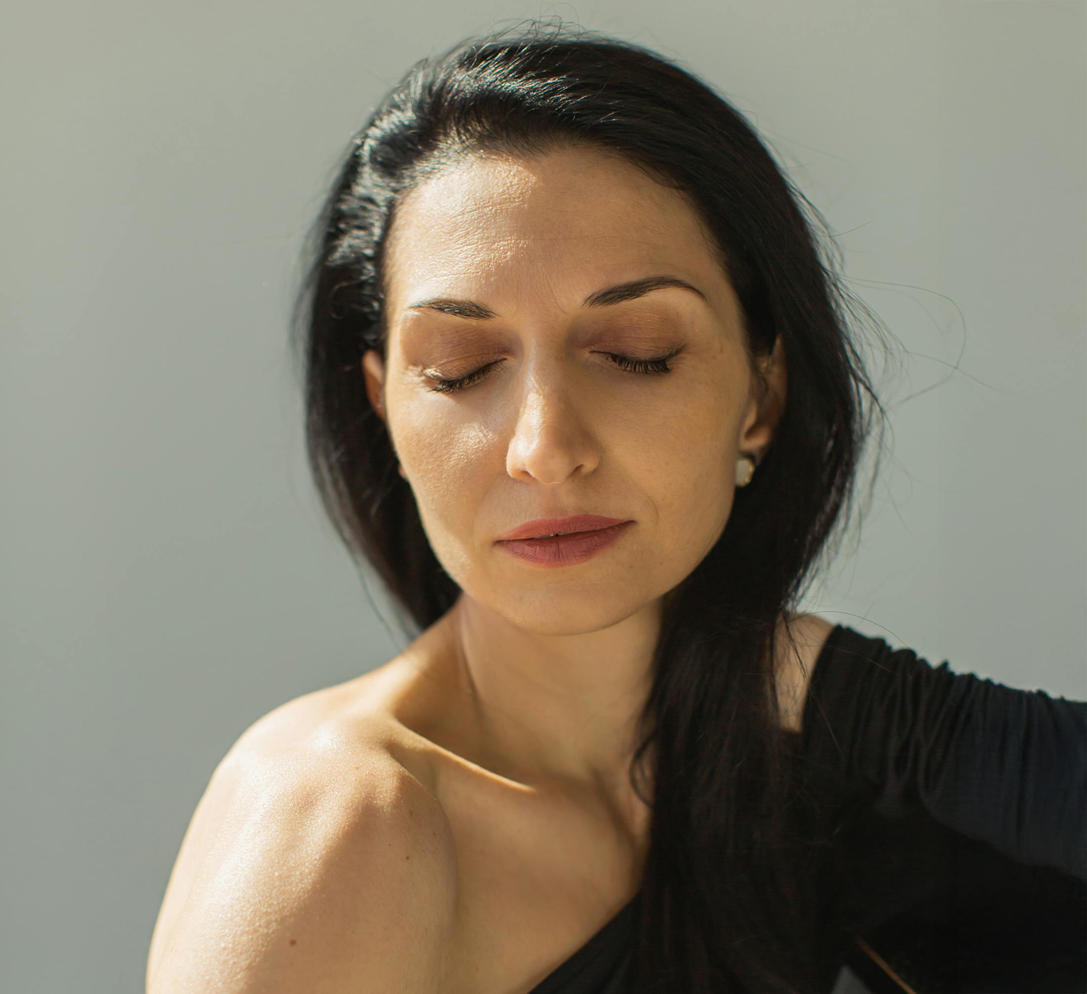 woman with dark black hair holding her neck with her eyes closed