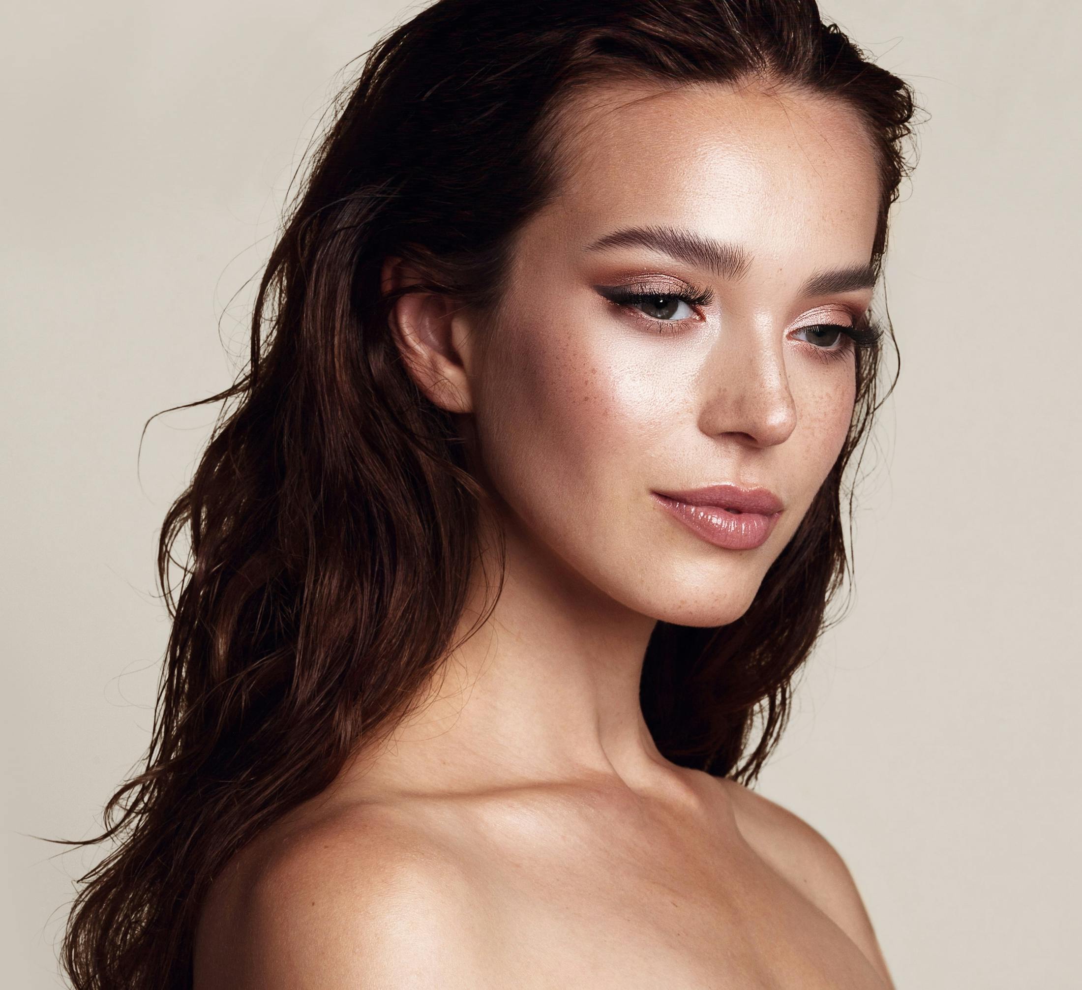 woman with brown hair and glowy makeup looking away from the camera