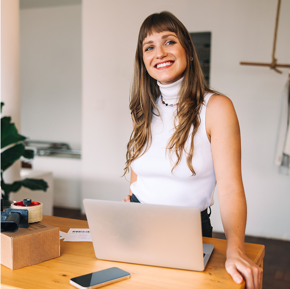 Program partnerski i lojalnościowy w sklepie internetowym Uśmiechnięta kobieta stojąca przy laptopie i korzystająca z programu partnerskiego w sklepie IdoSell.