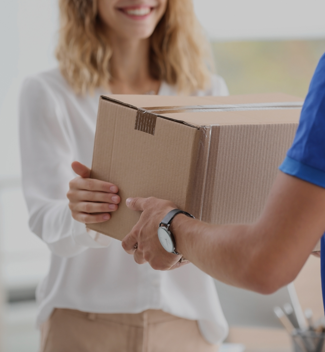 Uśmiechnięta kobieta odbierająca paczkę od kuriera.