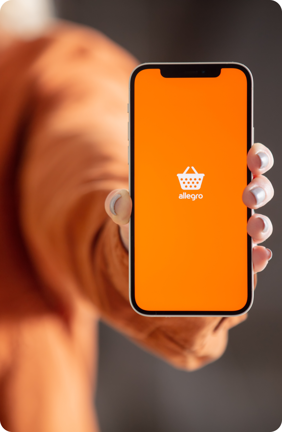 Smartfon trzymany w dłoni z pomarańczowym ekranem aplikacji Allegro i logo koszyka – symbol sprzedaży i reklam Allegro Ads w e-commerce.