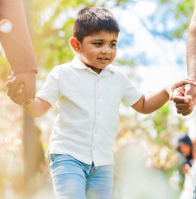 young boy walking while holding parents hands
