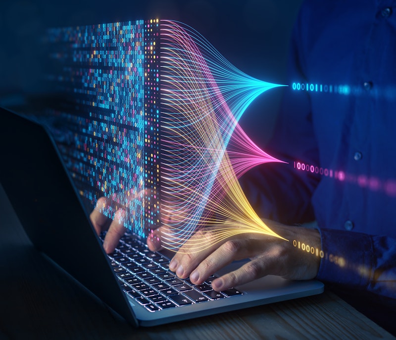 Person working on a laptop with colourful holographic data streams and binary code visualizations symbolising big data analysis and machine learning.