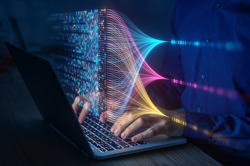 Person working on a laptop with colourful holographic data streams and binary code visualizations symbolising big data analysis and machine learning.
