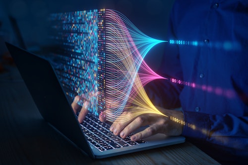 Person working on a laptop with colourful holographic data streams and binary code visualizations symbolising big data analysis and machine learning.