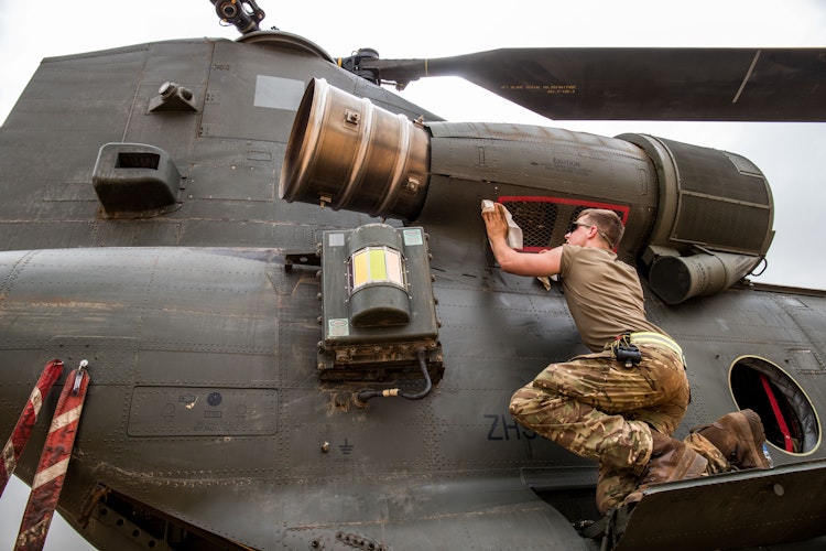 Soldier performing maintenance on a military helicopter engine intake.
