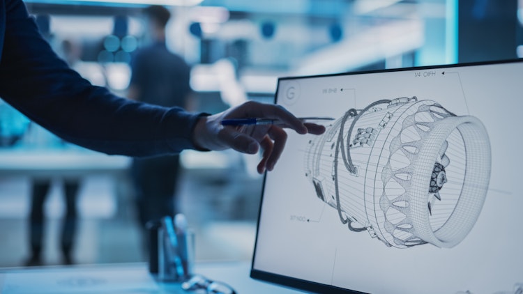 Engineer reviewing a 3D wireframe model of a jet engine on a computer screen in a high-tech design lab.