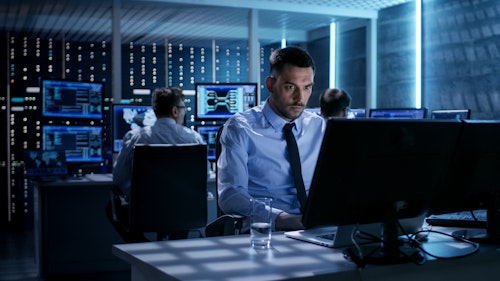 Focused cybersecurity analyst working in a high-tech operations center surrounded by multiple monitors displaying data and digital maps.