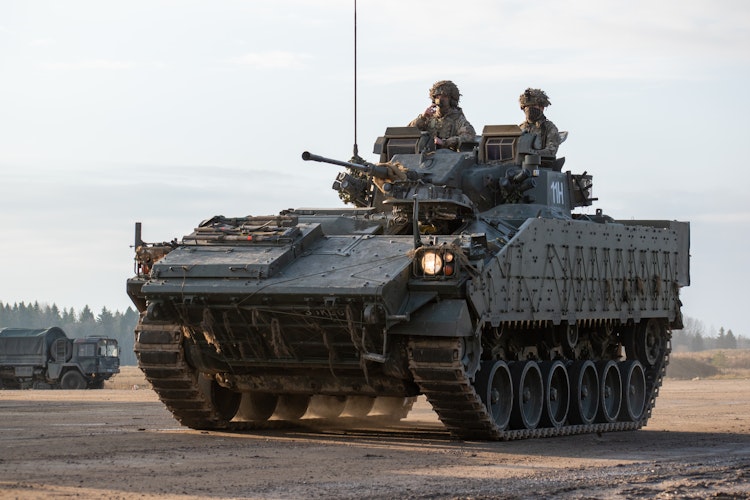 Military armoured vehicle with soldiers positioned on top during field operations.