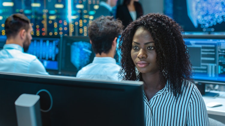 Focused cybersecurity analyst working at her computer in a high-tech operations center.