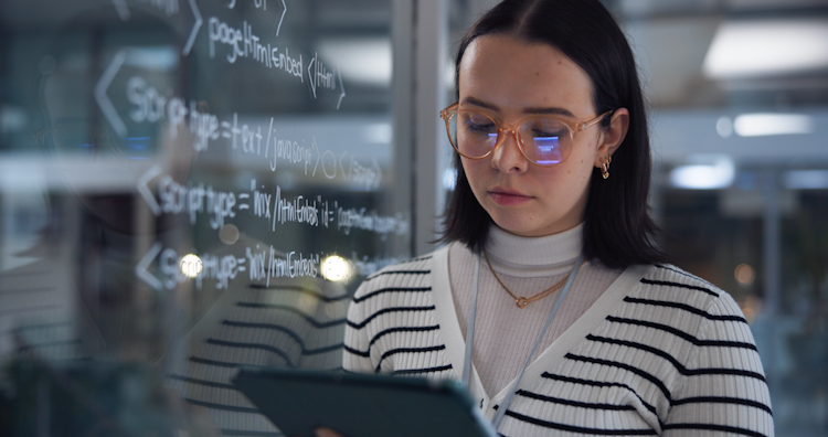 Focused developer reviewing code on a tablet beside a glass wall with programming scripts.