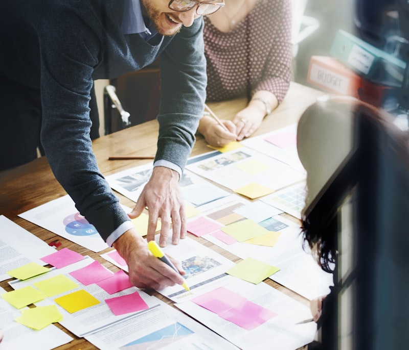 Business team collaborating around a table covered with documents, charts, and colorful sticky notes during a strategy planning session.