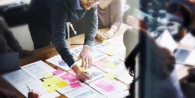 Business team collaborating around a table covered with documents, charts, and colorful sticky notes during a strategy planning session.