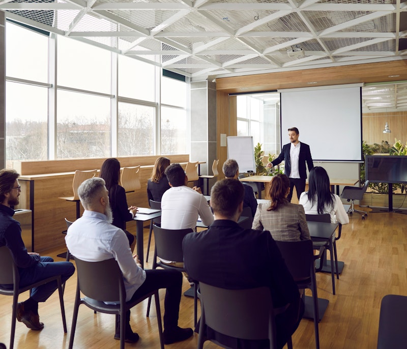 Business professional giving a presentation to a seated group in a modern conference room.