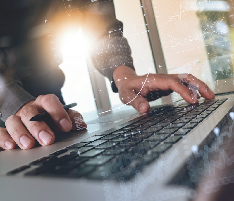 Close-up of hands typing on a laptop keyboard with overlaid digital graphics of charts, data, and analytics.