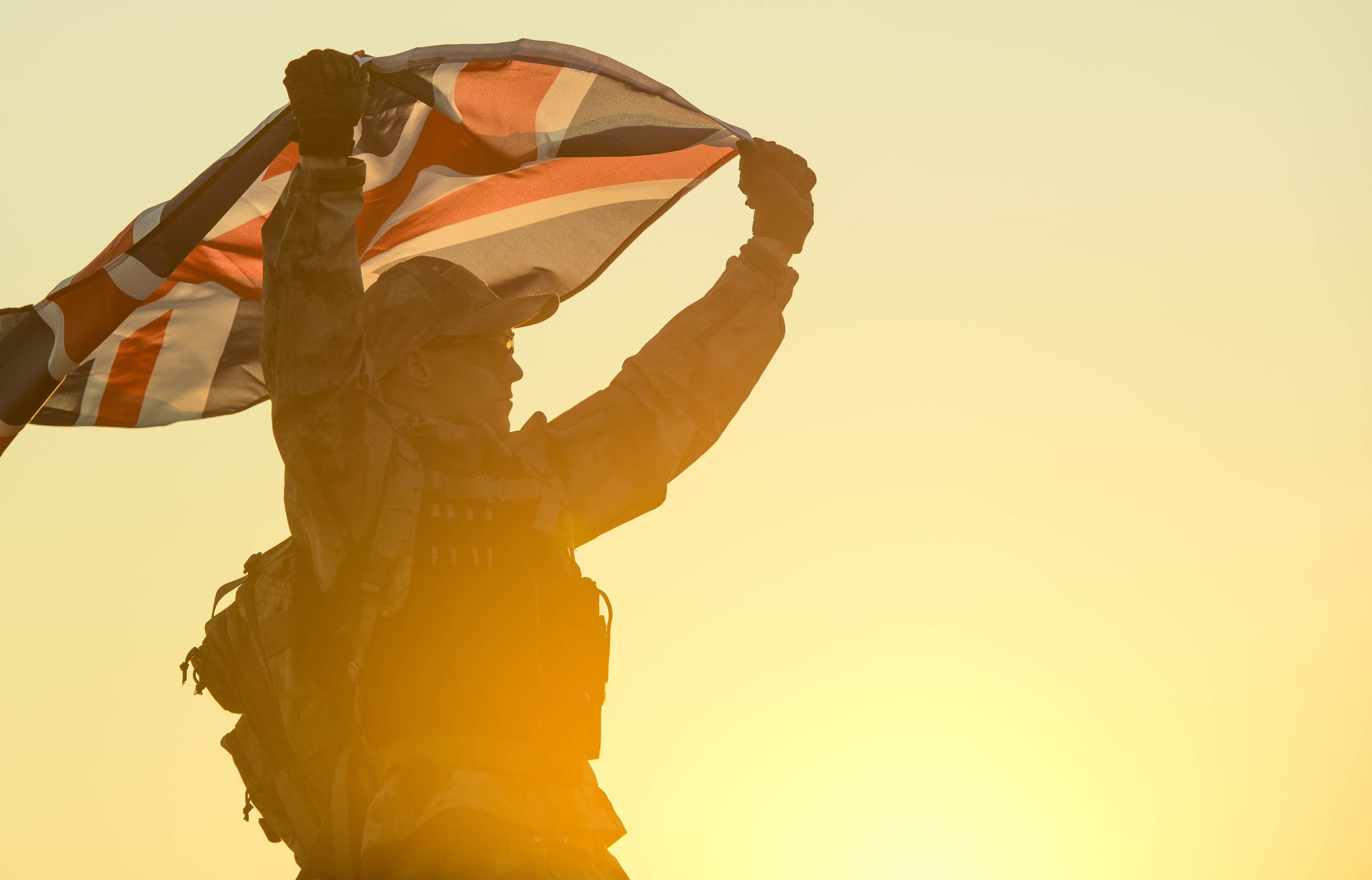 Silhouette of a soldier holding up a Union Jack flag against a golden sunset sky.