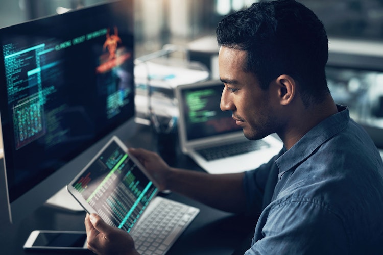 Cybersecurity professional analyzing code and threat data across multiple devices.